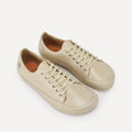 A pair of low-top leather barefoot dance sneakers in a light beige color, featuring matching beige laces and silver metal eyelets, displayed on a clean off-white background.