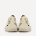 A pair of low-top leather barefoot dance sneakers in a light cream or beige color, shown from the front against a plain white background.