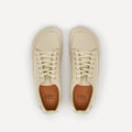 A pair of cream-colored leather lace-up barefoot dance sneakers with beige laces, silver eyelets and a black logo saying 