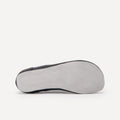 The bottom sole of a black leather barefoot dance sneaker, showing a light gray suede sole, photographed from a side profile against a clean off-white background.