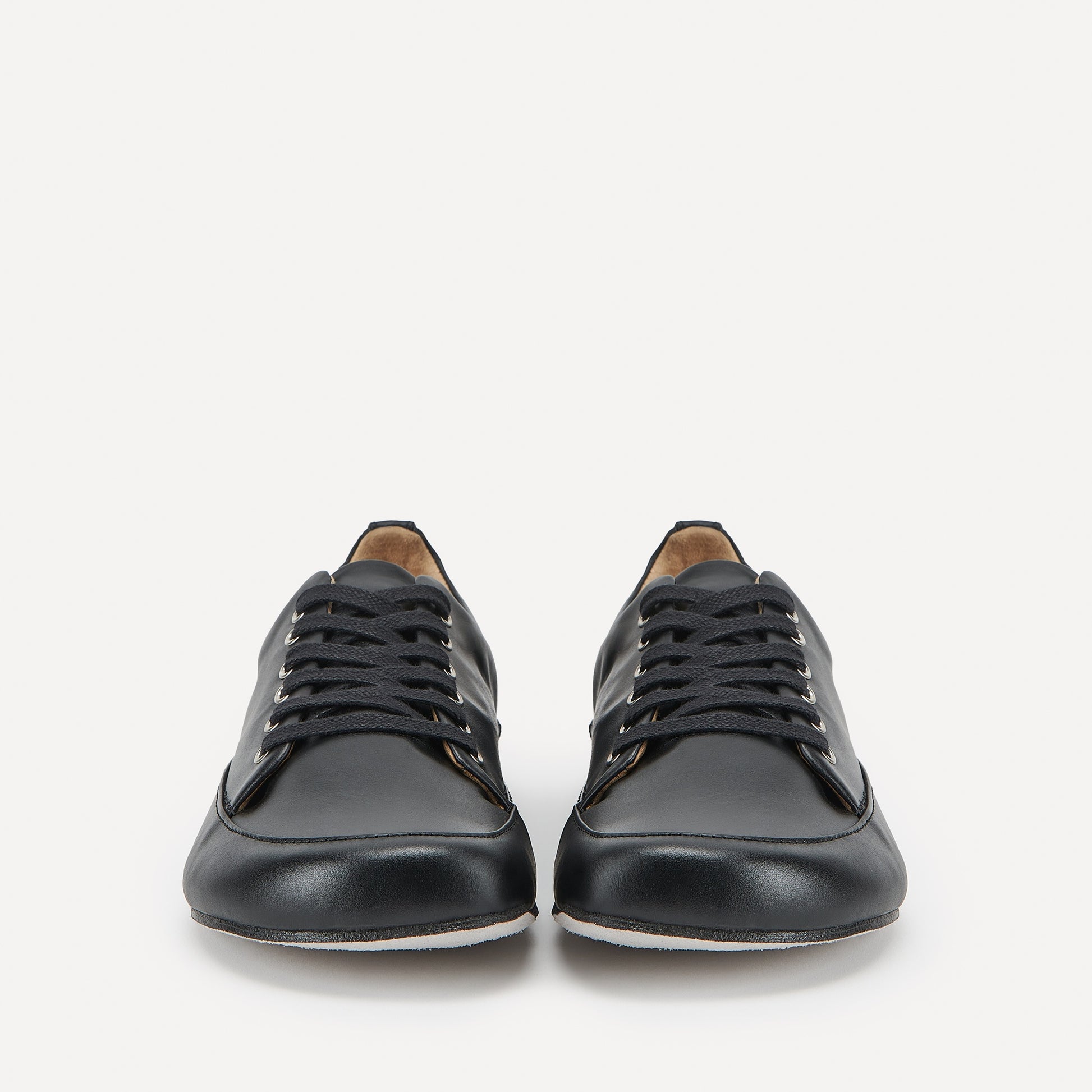 A pair of black leather low-top lace-up barefoot dance sneakers with a broad rounded toe box, photographed from the front against a clean white background.