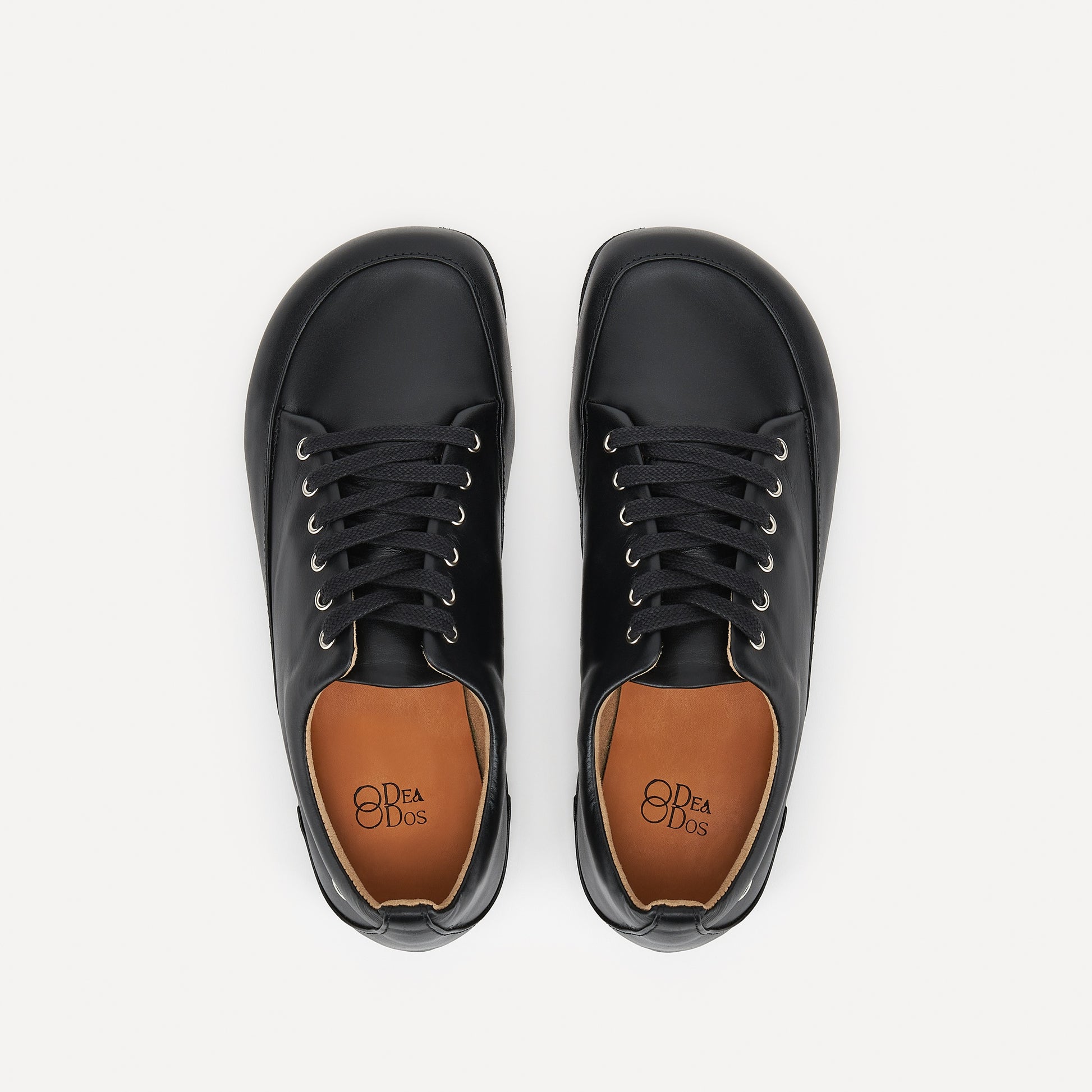 A pair of black leather lace-up barefoot dance sneakers  with black laces and silver eyelets, displayed on a clean off-white background.